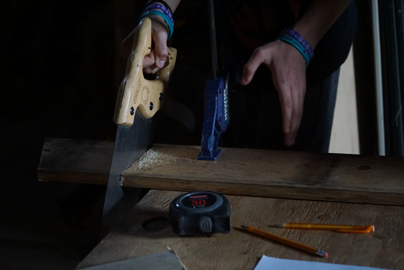 An image of a person sawing a piece of wood that is clamped to a table.