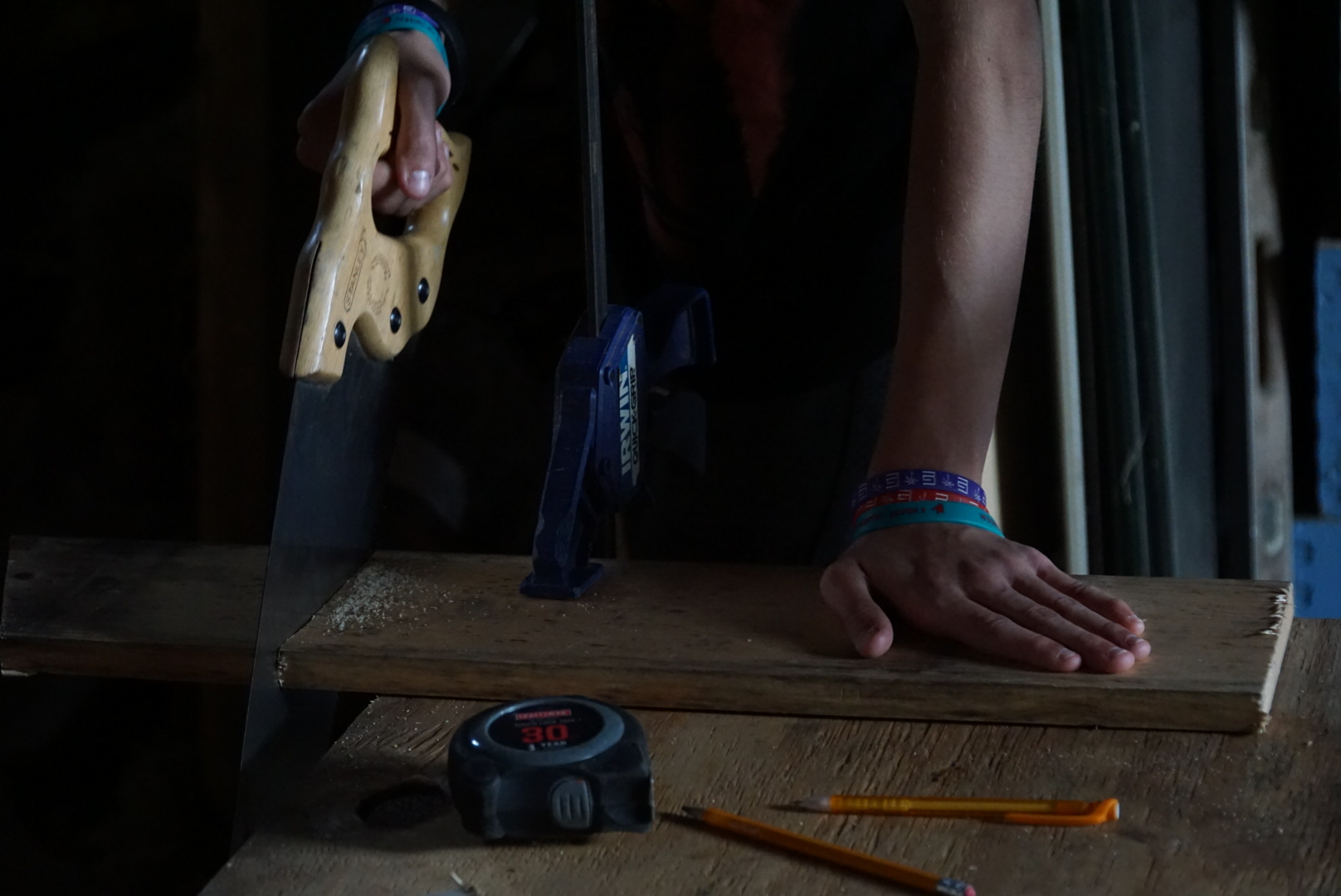 An image of a person sawing a piece of wood that is clamped to a table.