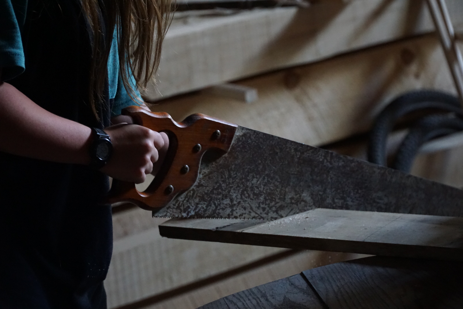 An image of a young adult using a saw to cut a piece of wood.