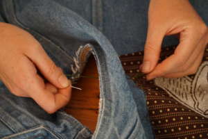 An image of someone sewing a patch onto a jean jacket.