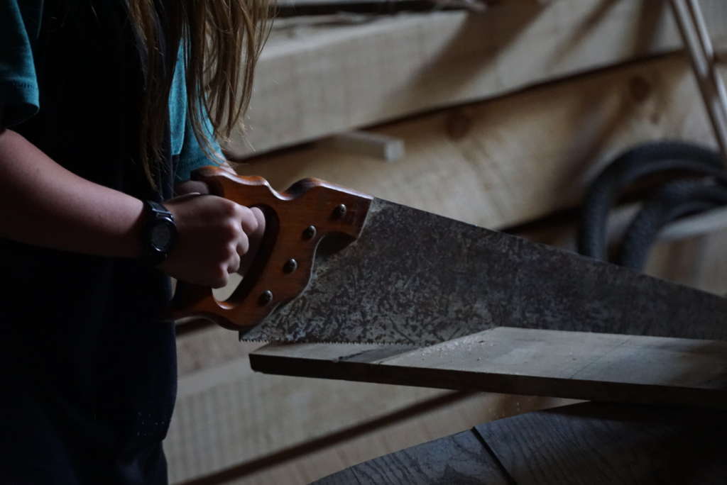 Person with long hair cutting wood with a hand saw